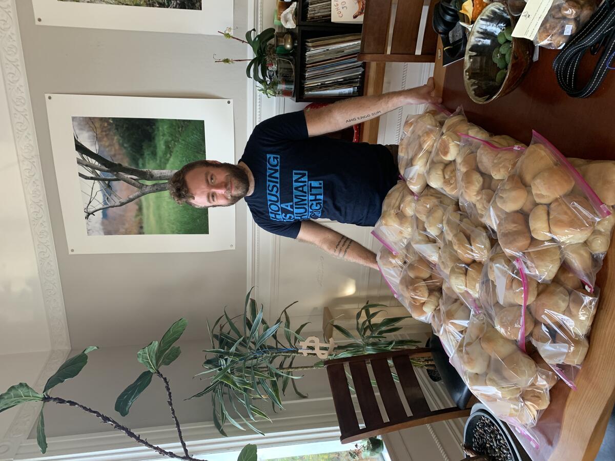 Student stands behind a table with many bread rolls in plastic bags.